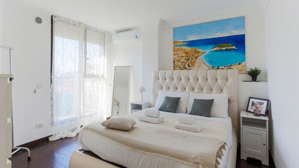 Een slaapkamer met een groot bed, een schilderij van een strand, een nachtkastje en een bedtafel.