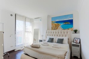A bedroom with a large bed, a painting of a beach, a bedside table, and a nightstand. - The Best Rent - Spacious apartment with balcony in viale Monza (Milano)