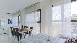 Een moderne hotelkamer met een groot bed, een zithoek met stoelen en grote ramen voorzien van transparante gordijnen.