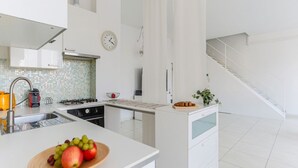 Een moderne keuken met witte kastjes, een betegelde achterwand, een roestvrijstalen spoelbak en een schaal met fruit op het aanrecht.