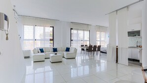 Een ruime woonkamer met een witte modulaire bank, een eethoek met tafel en stoelen, en een keuken met aanrecht en kasten.
