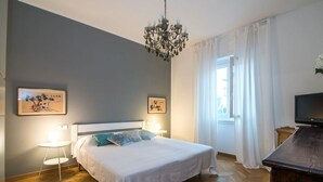 A bedroom with a bed, bedside tables, a chandelier, artwork on the walls, and a television on a wooden cabinet. - The Best Rent - Two-bedroom apatment in Milan (Milano)