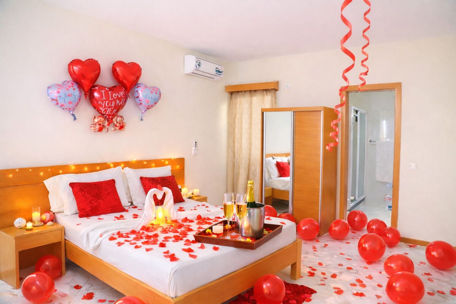 A hotel room with a bed, a bedside table, a nightstand, a mirror, and a door.