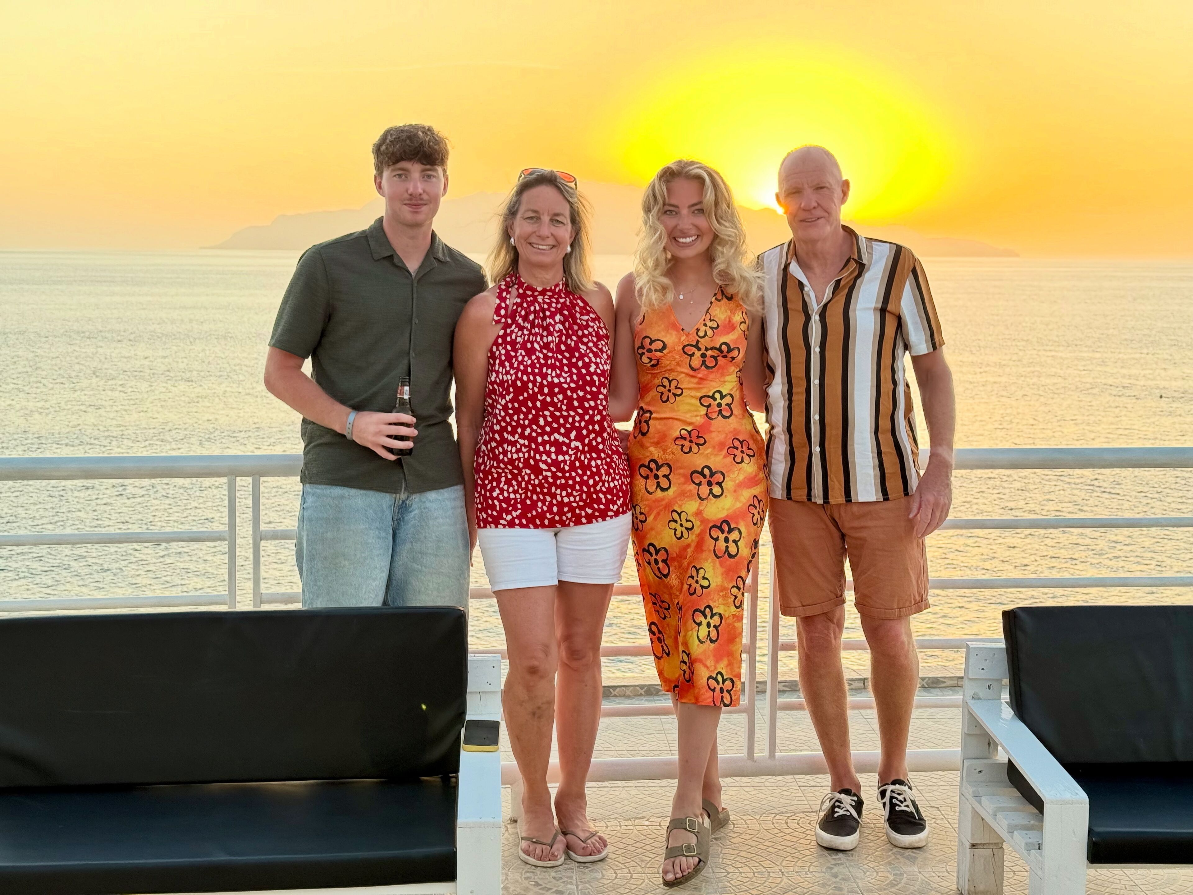 A group of people standing on a balcony with a view of the sea and a sunset.