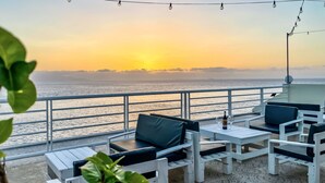 A balcony with white furniture, a view of the sea, and a sunset. - Cruzeiro Guest House (São Filipe)