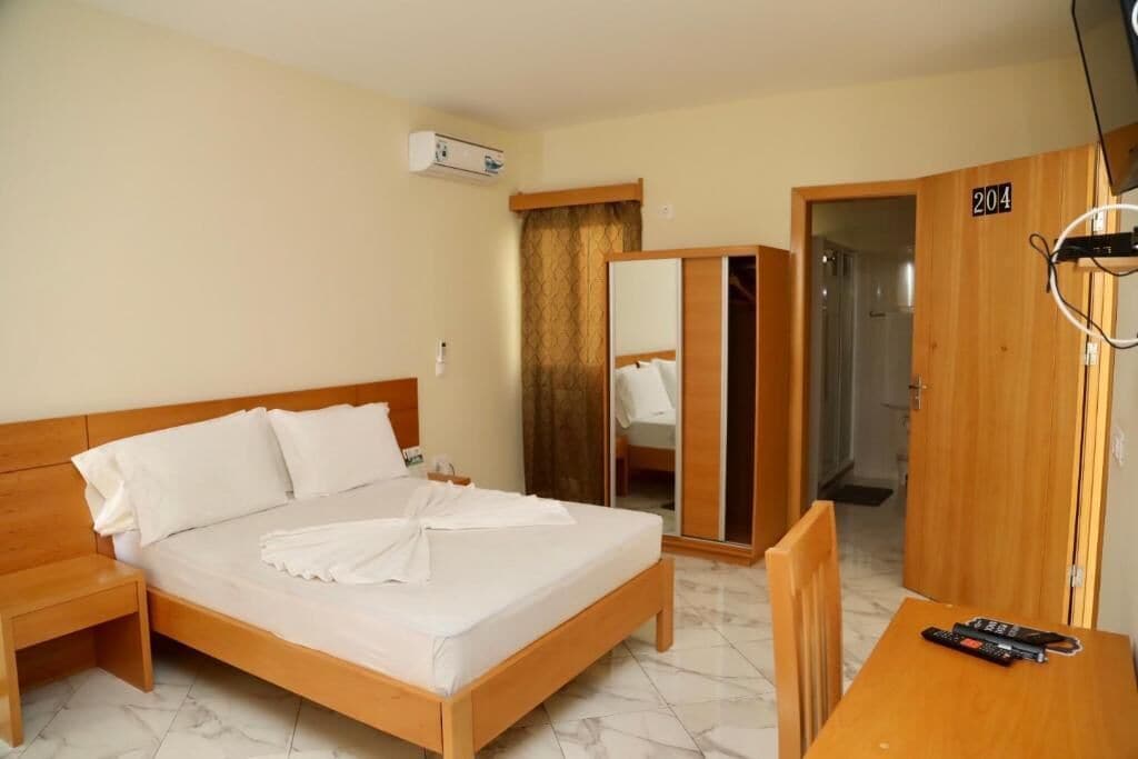 A hotel room with a wooden bed, a bedside table, a wardrobe, and a TV.