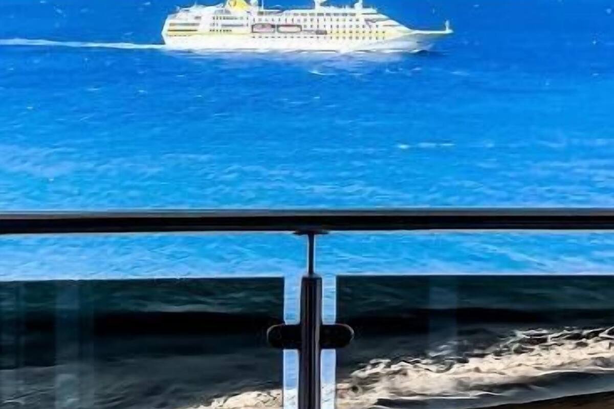 On aperçoit au loin un navire de croisière, avec une vue dégagée sur l’océan et une île montagneuse en arrière-plan.