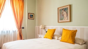 Un dormitorio con una cama grande, dos almohadas, una mesita de noche, una lámpara y un cuadro en la pared.