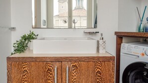 Ein Badezimmer mit Holzwaschtisch, einem weißen Waschbecken, einem Spiegel und einer Waschmaschine.