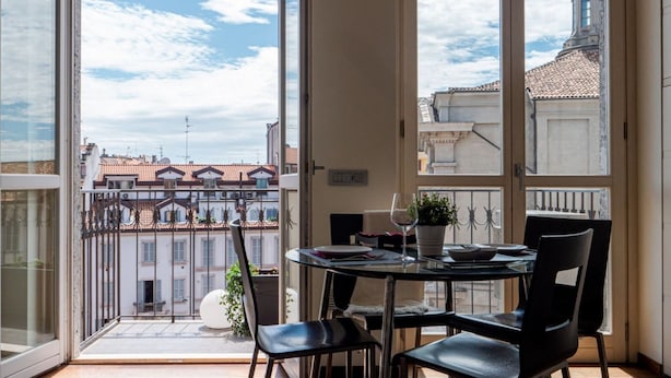 Ein Balkon mit Tisch und Stühlen, einem Blumentopf und Blick auf Gebäude sowie einen klaren Himmel.