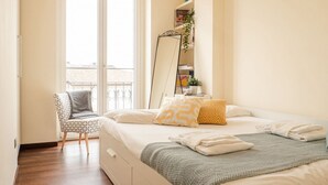 Ein Schlafzimmer mit einem Bett, einem Sessel, einem großen Spiegel und Blick ins Freie.