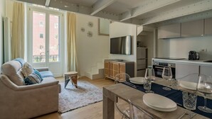 A modern living room with a sofa, a dining table set with plates and glasses, a kitchen with a TV and appliances, and a staircase leading to an upper floor. - The Best Rent - Lovely loft with balcony near Piazza Vetra (Milano)