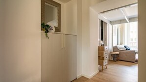 A modern, well-lit room with a wooden floor, a white wardrobe, a small desk with drawers, and a sofa in the background. - The Best Rent - Lovely loft with balcony near Piazza Vetra (Milano)
