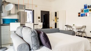 A modern hotel room with a bed, a desk, and a kitchenette.