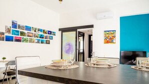A modern kitchen with a dark countertop, a dining area with chairs, and a wall adorned with photographs and artwork.