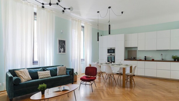 Un salon moderne avec un canapé vert, un fauteuil rouge et un coin repas comprenant des chaises blanches et une table.