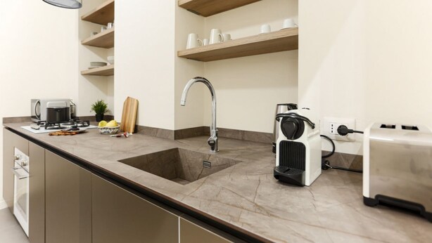 A modern kitchen with a built-in sink, a coffee maker, a toaster, and wooden shelves above the counter. - The Best Rent - Flat with 1 bedroom in Moscova area (Milano)