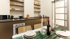 A compact kitchen with a microwave, stove, and shelves with dishes and jars. There's a dining table with a candle and wine bottle. - The Best Rent - Flat with 1 bedroom in Moscova area (Milano)