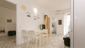 A modern, well-lit room with a dining area featuring a white table and chairs, a wooden cabinet, and a television. The floor has a unique geometric pattern. - The Best Rent - Two bedrooms apartment near metro station Maciachini (Milano)