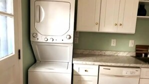 Een compacte keuken met een wasmachine en vaatwasser, witte kastjes en een marmeren aanrechtblad.