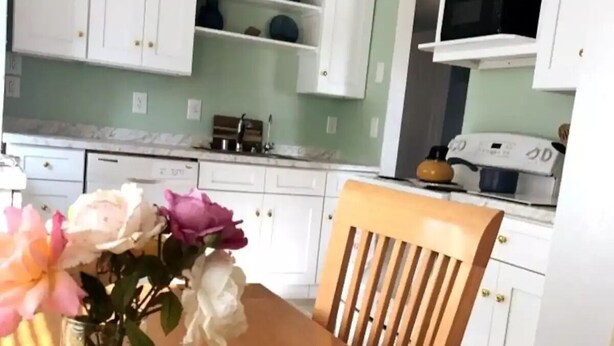 Een keuken met witte kastjes, een houten stoel en een bloemenvaas op de tafel.