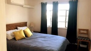Een slaapkamer met een bed, een stoel, een raam met gordijnen en een airconditioning.