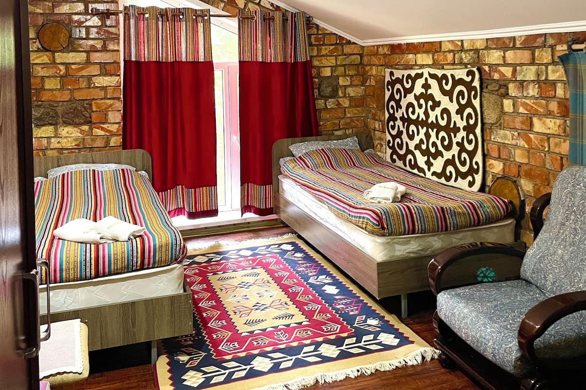 A cozy room with a bed, a chair, a patterned rug, and a stone wall.