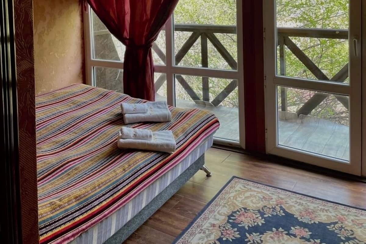 A room with a bed, a window with curtains, and a view of greenery outside.