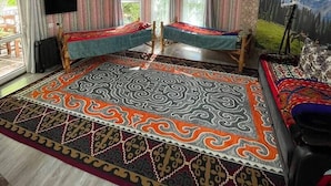 A room with a large patterned rug, two beds, a ceiling fan, and a painting on the wall. - Touristic Complex Chychkan (Bala-Chychkan)