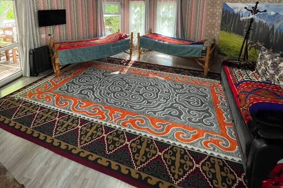 A room with a large patterned rug, two beds, a ceiling fan, and a painting on the wall.