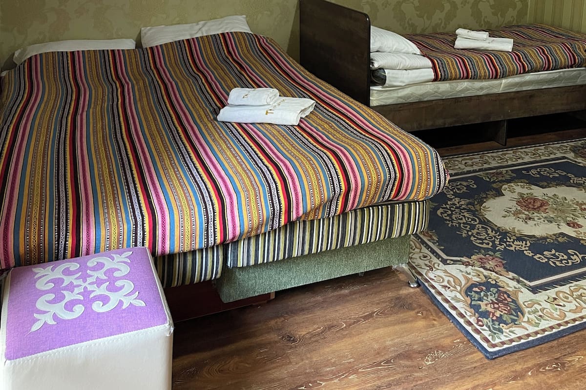 A bedroom with two beds, a wooden floor, a patterned rug, and a decorative wall hanging.