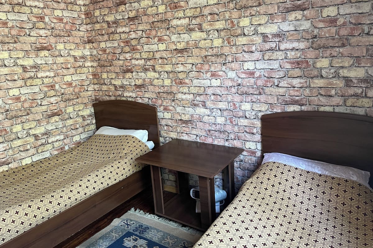 A room with two wooden beds against a brick wall, a small wooden table, and a patterned rug.