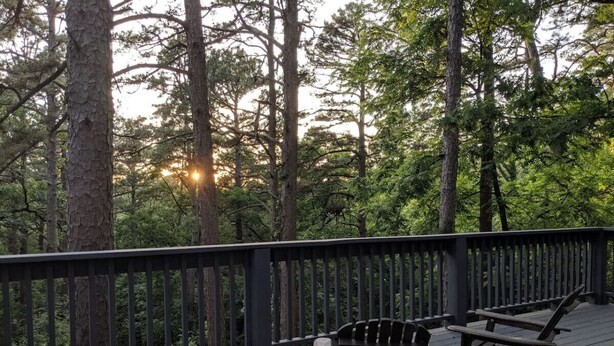 Une terrasse en bois, agrémentée de deux fauteuils Adirondack, entourée d’une rambarde noire et offrant une vue sur une zone boisée.