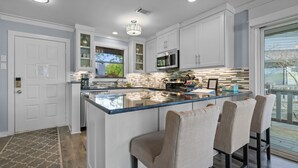 A modern kitchen with white cabinets, a large island with bar stools, a built-in microwave, and a window overlooking the outdoors. - The VIEW @ Farr Shores! (Hot Springs)
