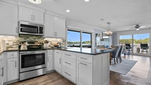 A modern kitchen with white cabinetry, stainless steel appliances, and a large island. - The VIEW @ Farr Shores! (Hot Springs)
