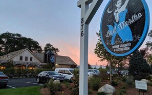 A sign for Bad Martha Farmer's Brewery & Tasting Room with a rustic building in the background.