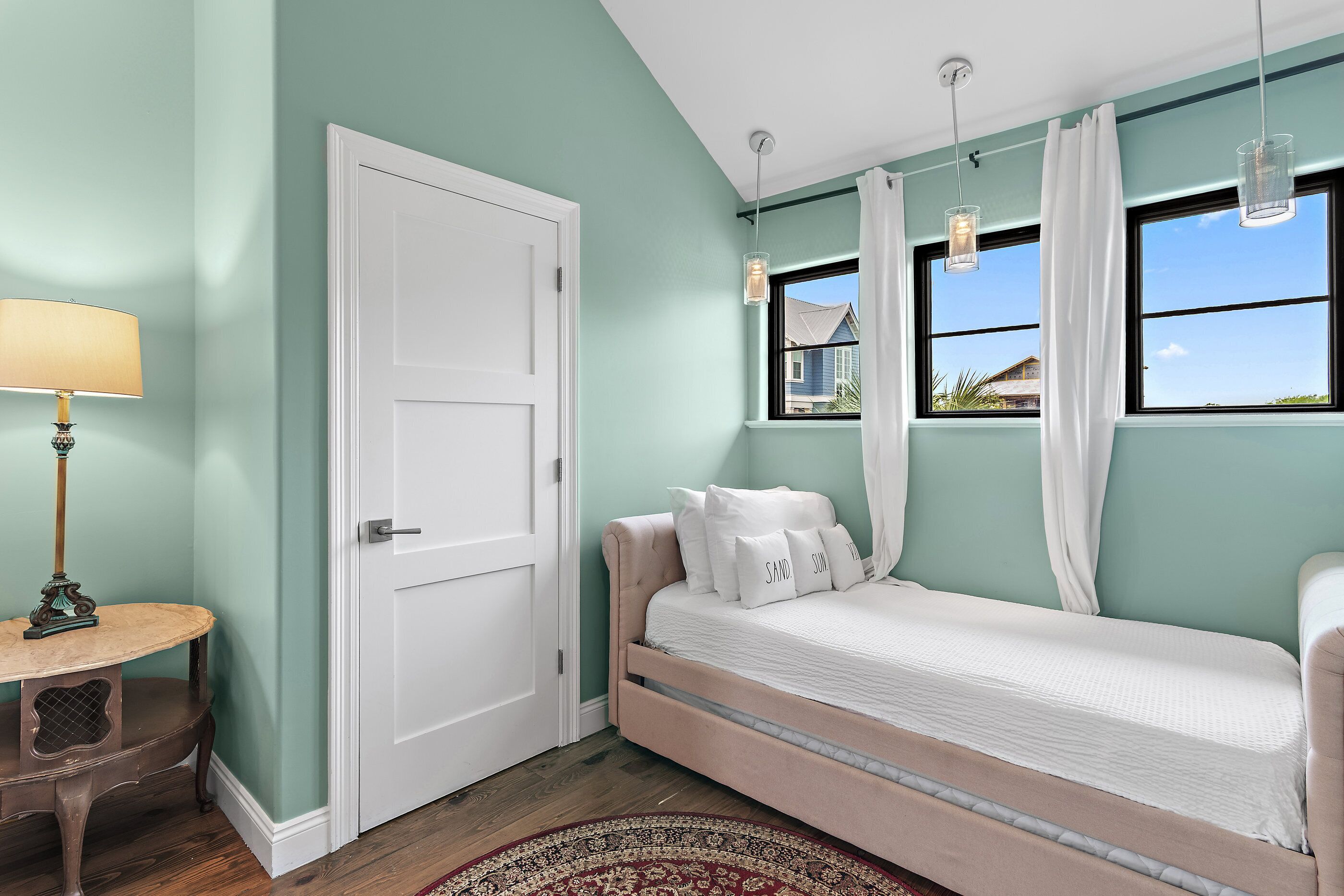 Un dormitorio con cama, puerta, lámpara y ventana con cortinas.