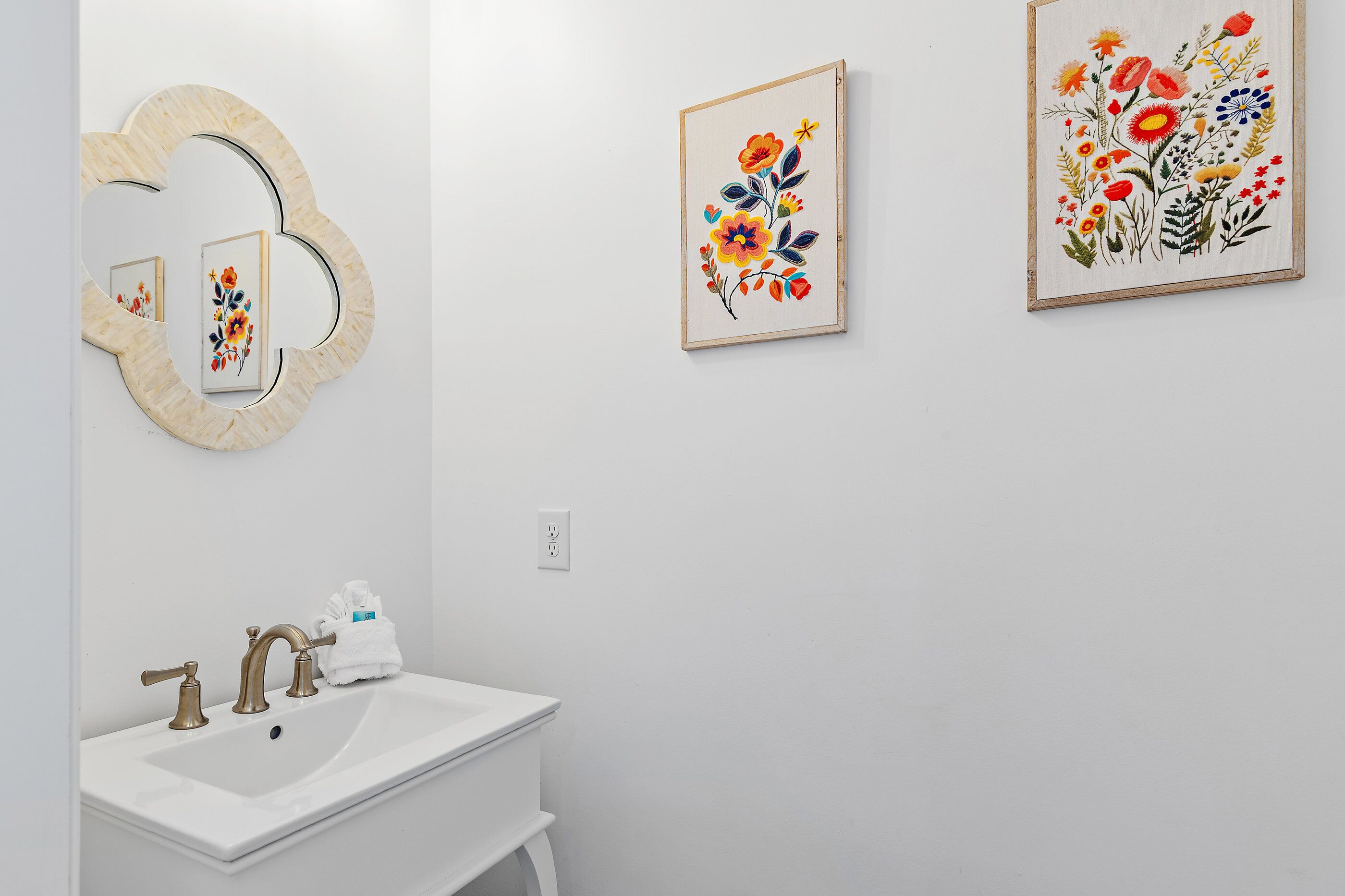 A bathroom with a sink, mirror, and two framed floral artworks on the wall.