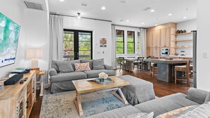 A modern living room with a sofa, coffee table, and a kitchen area with wooden cabinets and a bar.