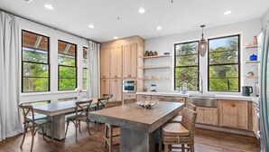 A kitchen with a central island, wooden cabinets, and large windows with a view of greenery.