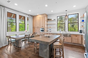 A kitchen with a central island, wooden cabinets, and large windows with a view of greenery.