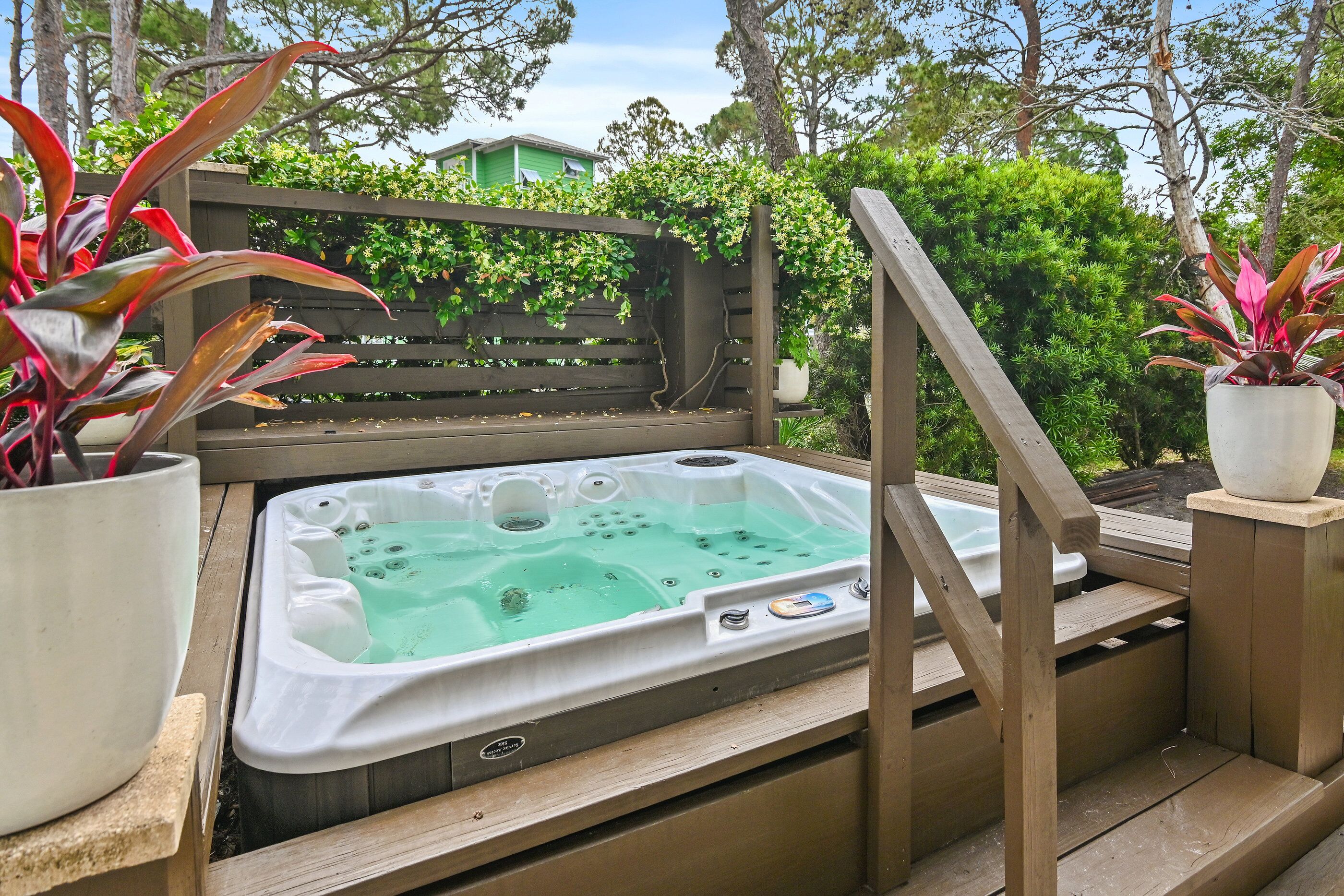 Un bain à remous sur une terrasse en bois, avec une clôture en bois et des plantes en pot.