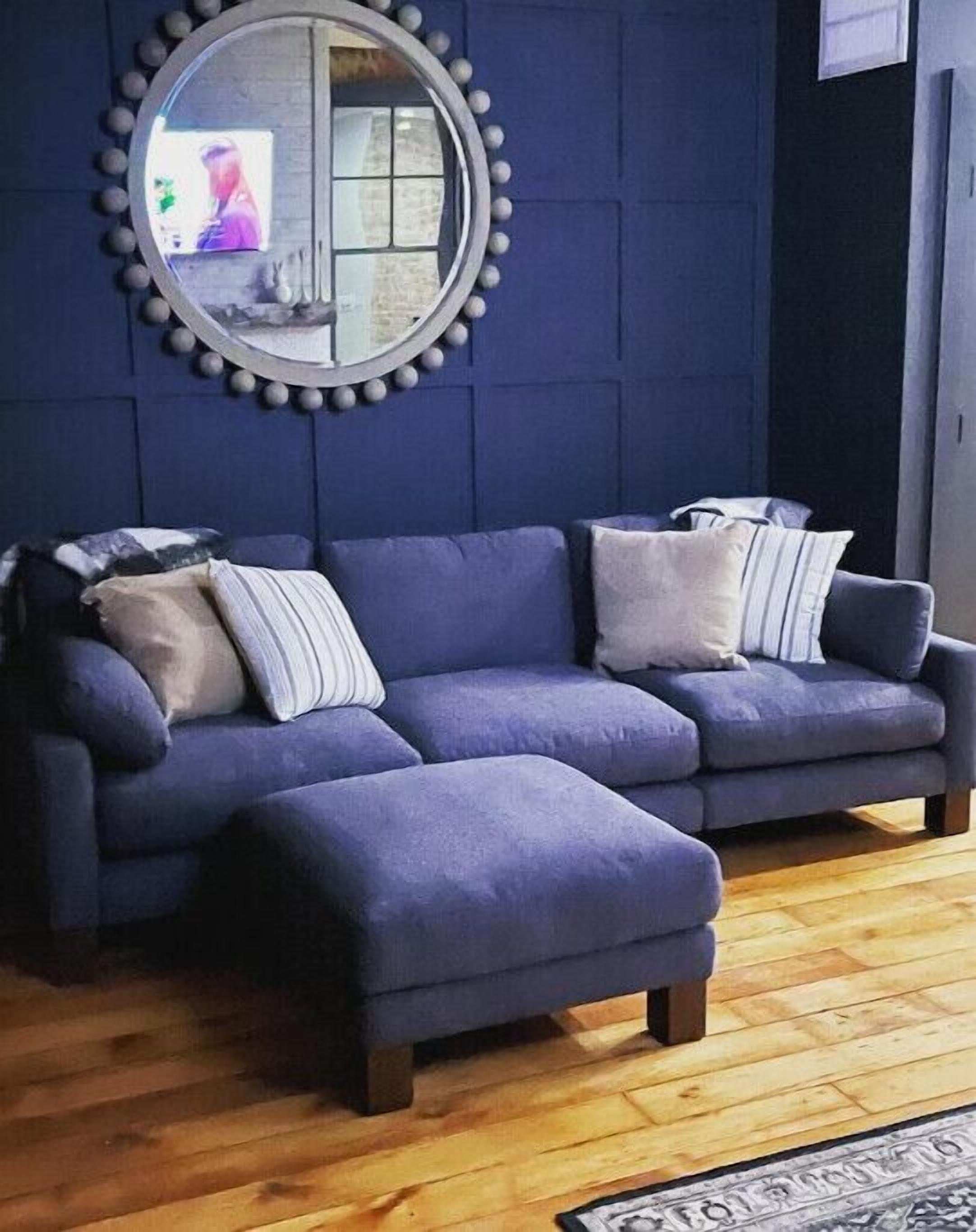 A modern living room with a blue sectional sofa, a round mirror with a decorative frame, and a wooden floor.