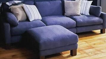 A modern living room with a blue sectional sofa, a round mirror with a decorative frame, and a wooden floor.