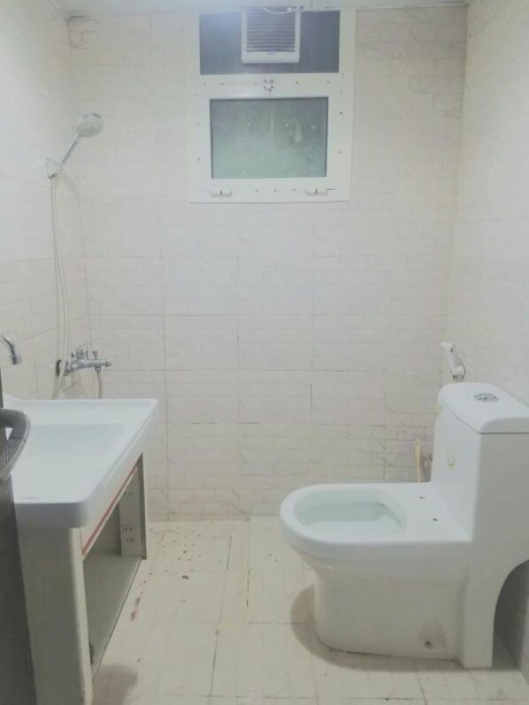 Casa de banho pequena e simples, com sanita, lavatório e chuveiro.