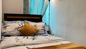 Una cama con ropa de cama floral, un almohadón amarillo y una lámpara de noche.