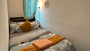 Un dormitorio con cama, ropa de cama floral, una mesita de noche, una lámpara y un cuadro colgado en la pared.