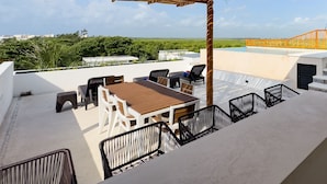 A rooftop terrace with a wooden table and chairs, a pool, and a view of the landscape. - Newly build 2 bedroom, luxury apartment a few steps from beach. (Puerto Morelos)