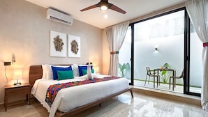 A hotel room with a large bed, a nightstand, a ceiling fan, and a sliding glass door leading to an outdoor area with a table and chairs. - Newly build 2 bedroom, luxury apartment a few steps from beach. (Puerto Morelos)