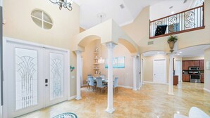 A spacious interior with a dining area, kitchen, and a balcony with decorative railings. - Private Villa | Heated Pool + Hot Tub + Sleeps 20 (Port St. Lucie)